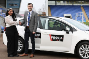 A man and a women shaking hands in front of a white Veezu car