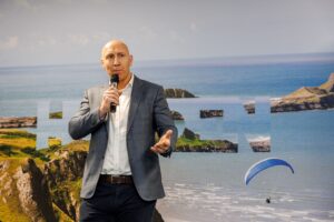 Man talking into a mic in front of a background of the sea