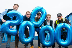 Group of people standing with blue balloons in the shape of 20,000