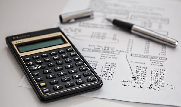 A black calculator on a white desk on top of some papers with maths calculations.